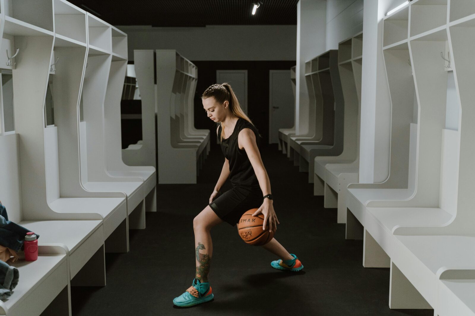 A female basketball player practicing dribbling in a modern indoor locker room.